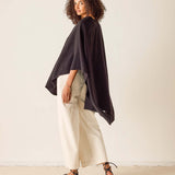 Woman wearing a black oversized top and white pants against a plain background