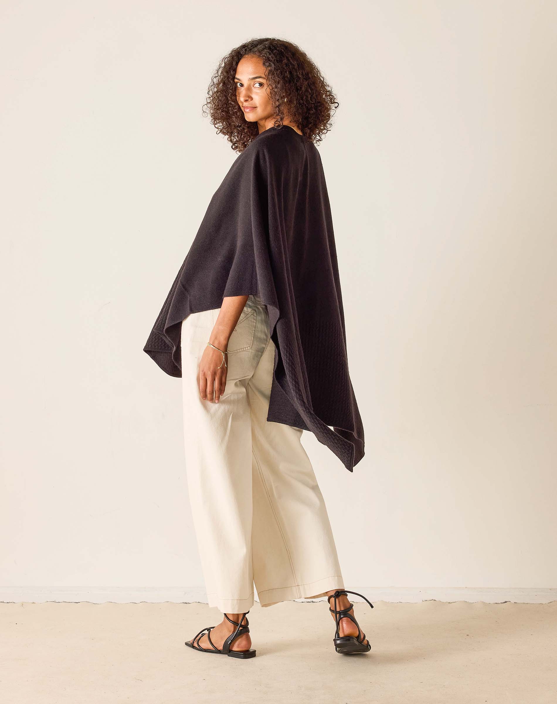 Woman wearing a black oversized top and white pants against a plain background