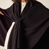 Person wearing a black shawl over a white outfit against a neutral background