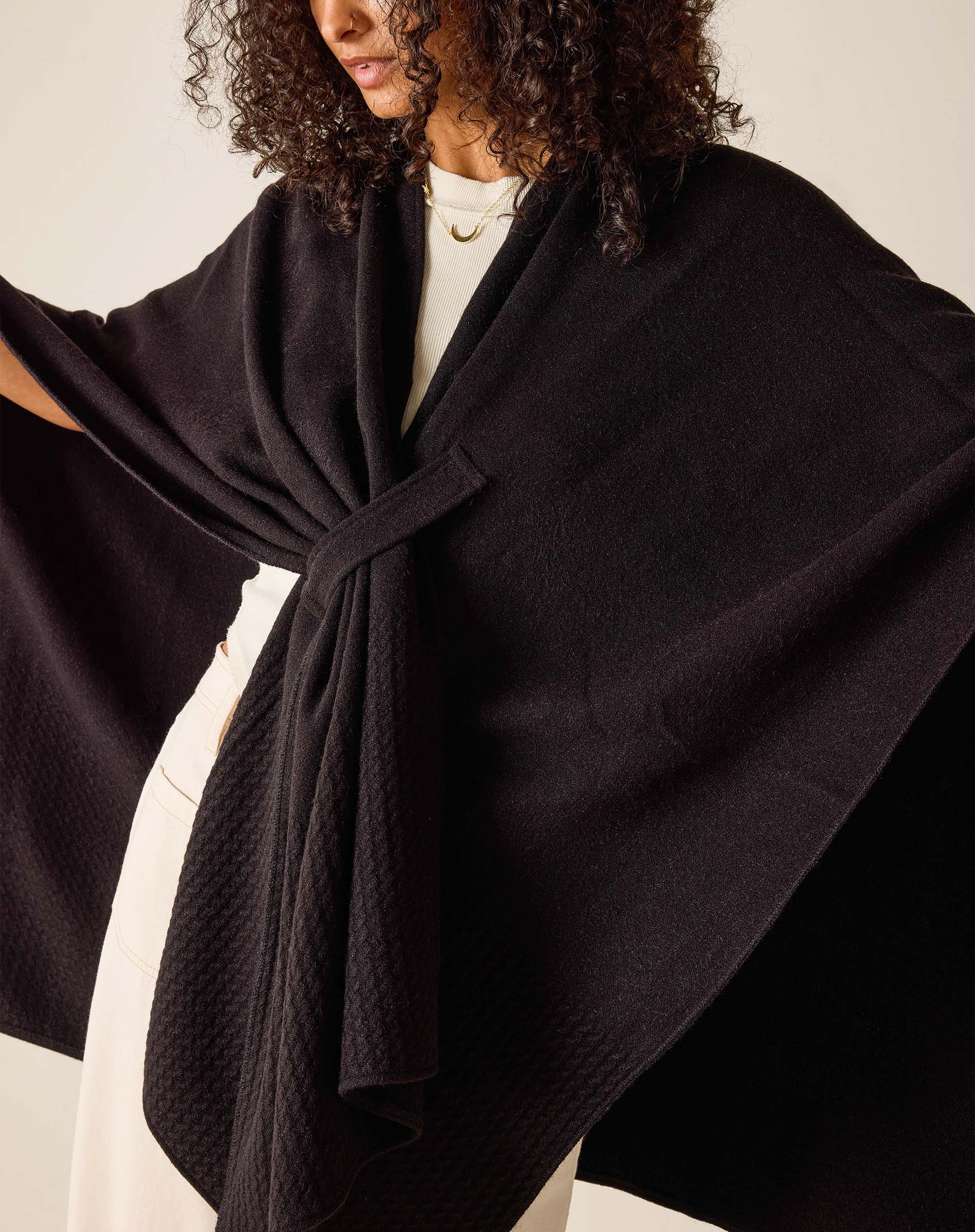 Person wearing a black shawl over a white outfit against a neutral background