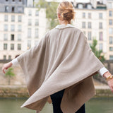 Person wearing a beige poncho in an urban setting with buildings and water in the background
