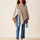 Woman wearing a beige poncho over a white shirt with blue jeans on a plain background