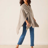 Woman wearing a beige poncho over a blue top and jeans on a plain background