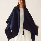 Woman wearing a navy blue poncho over a white outfit on a light background