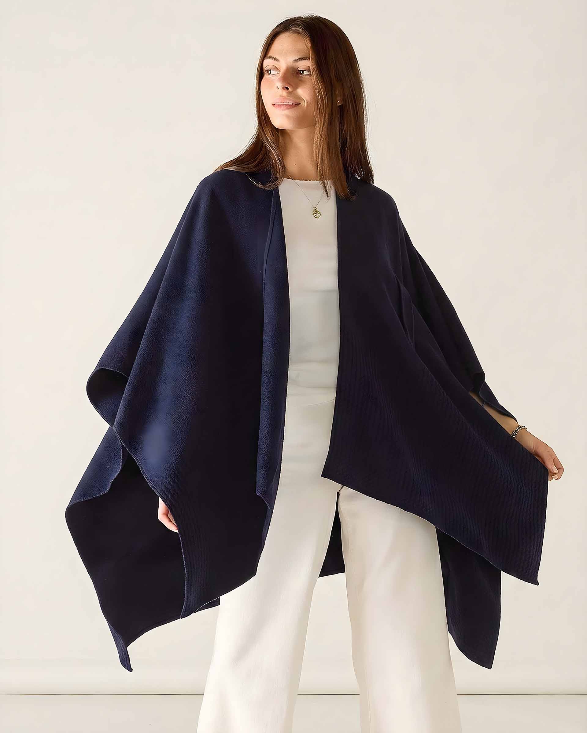 Woman wearing a navy blue poncho over a white outfit on a light background