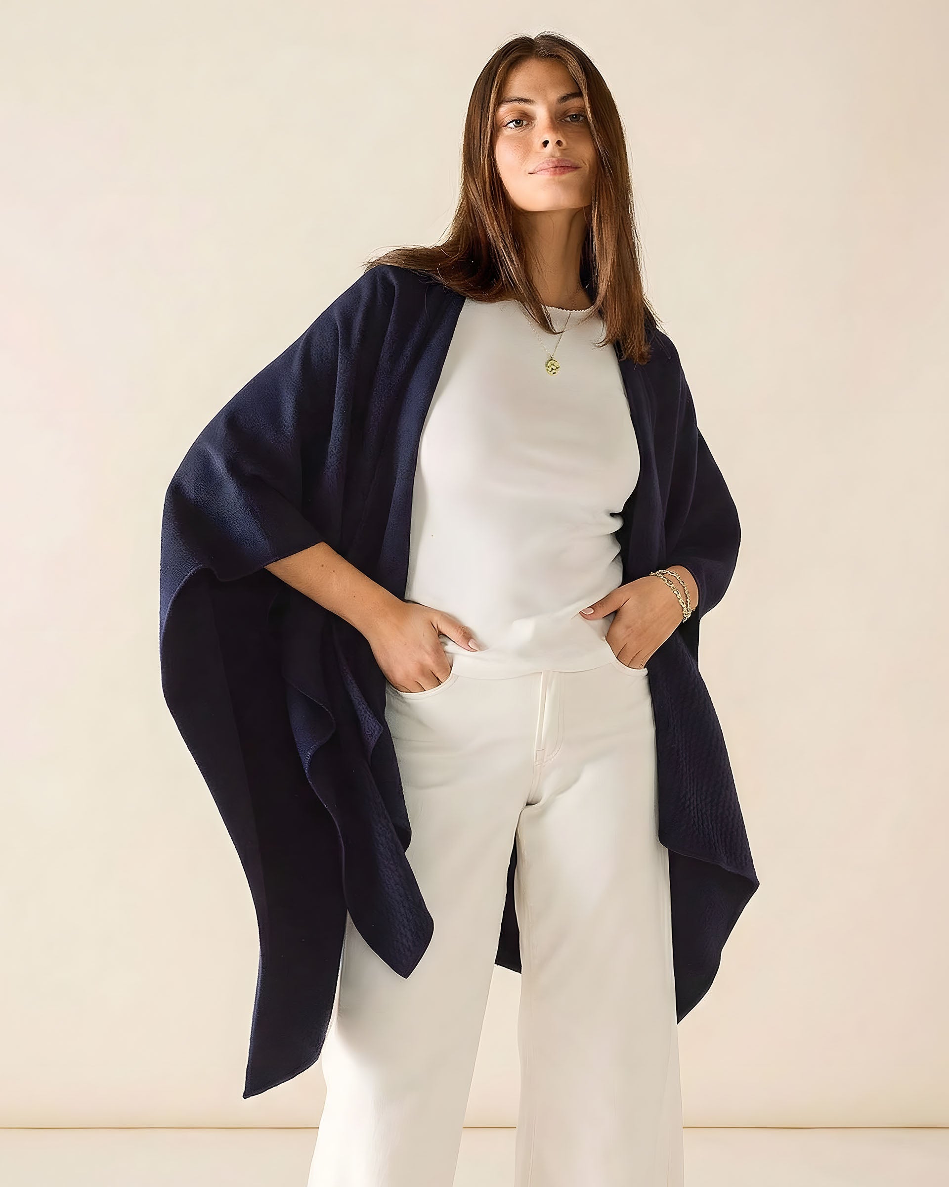 Woman wearing a navy blue cardigan over a white outfit on a beige background