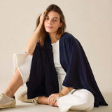 Woman sitting on a light-colored floor wearing a navy blue shawl over a white outfit.