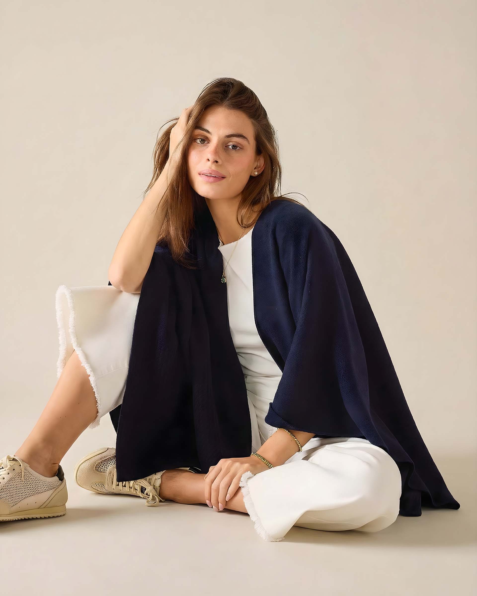 Woman sitting on a light-colored floor wearing a navy blue shawl over a white outfit.