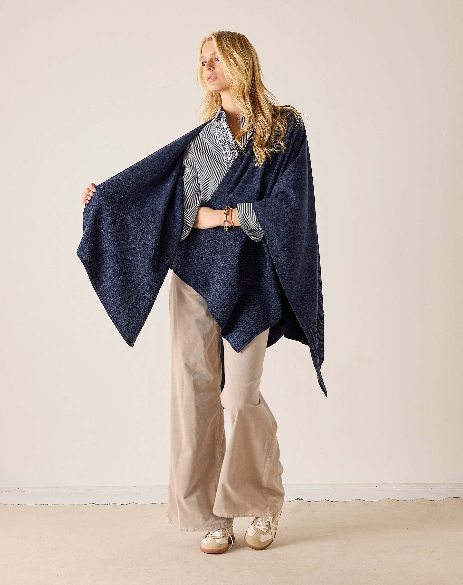 Navy blue waffle-texture travel wrap worn over a grey top and beige wide-leg trousers.