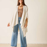 Woman wearing a beige cardigan, brown top, blue jeans, and brown shoes against a white background