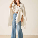Woman wearing a white poncho and blue jeans against a plain background