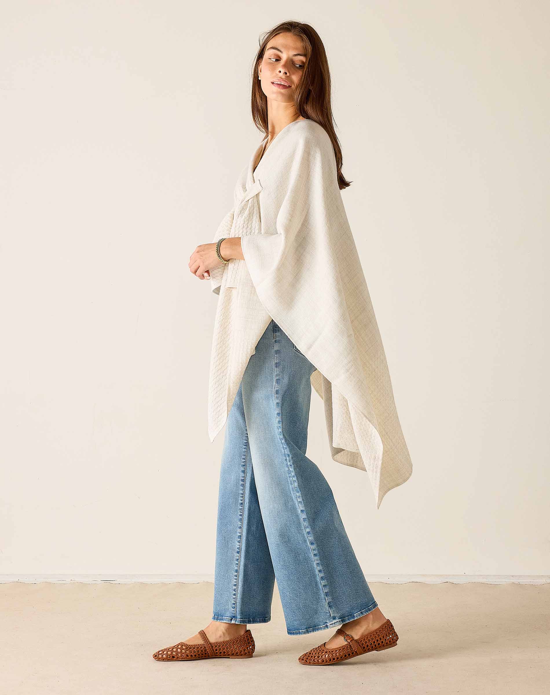 Woman wearing a white top and blue jeans against a plain background