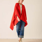 Woman wearing a red poncho, white shirt, blue jeans, and beige sneakers on a plain background