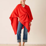 Woman wearing a red poncho over a white shirt and blue jeans on a beige background