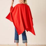 Woman wearing a red poncho and blue jeans against a beige background