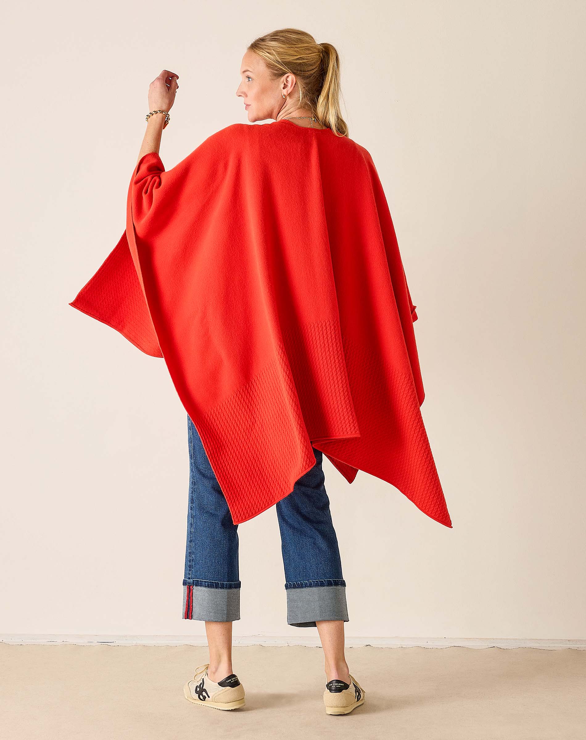 Woman wearing a red poncho and blue jeans against a beige background
