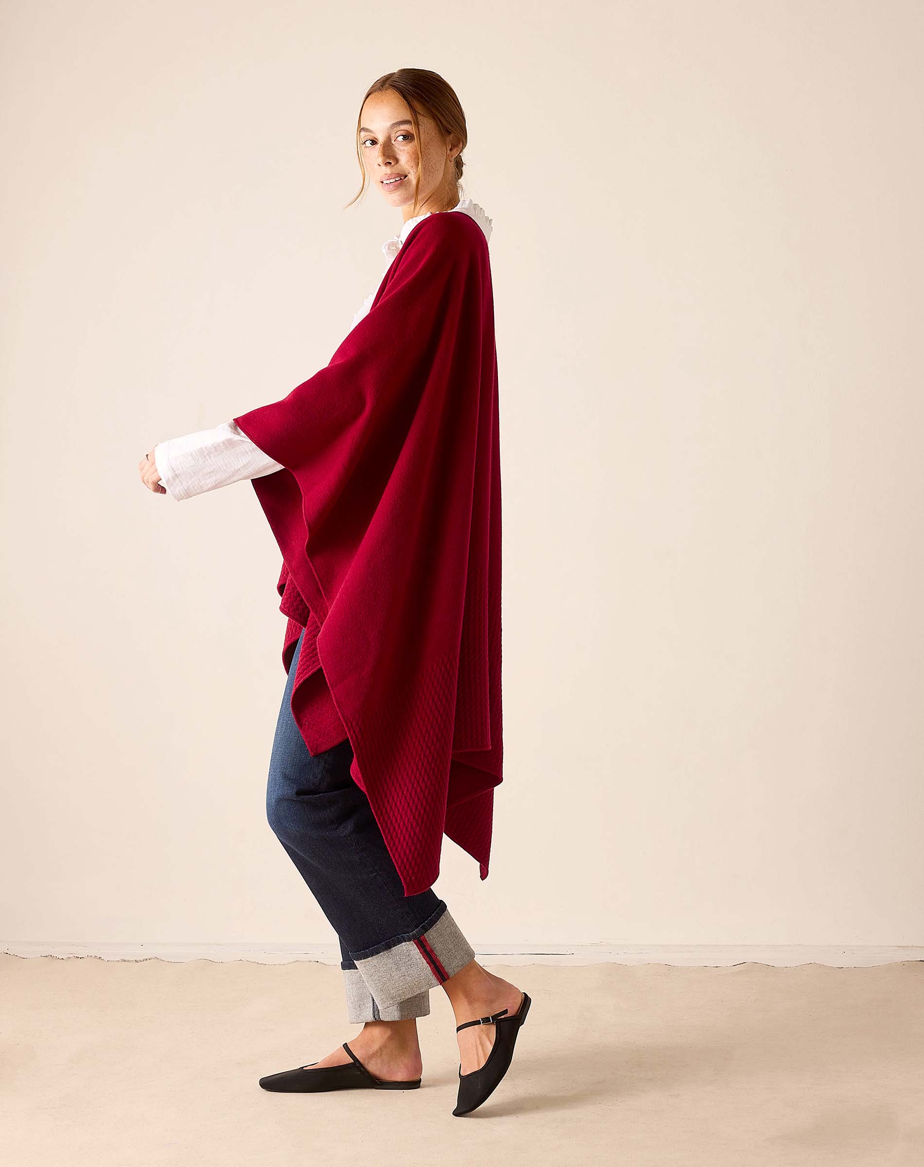 Wine colored ribbed knit travel wrap worn over a white long-sleeved top and dark pants.