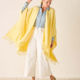 Woman wearing a yellow scarf with white pants and a light blue shirt on a beige background