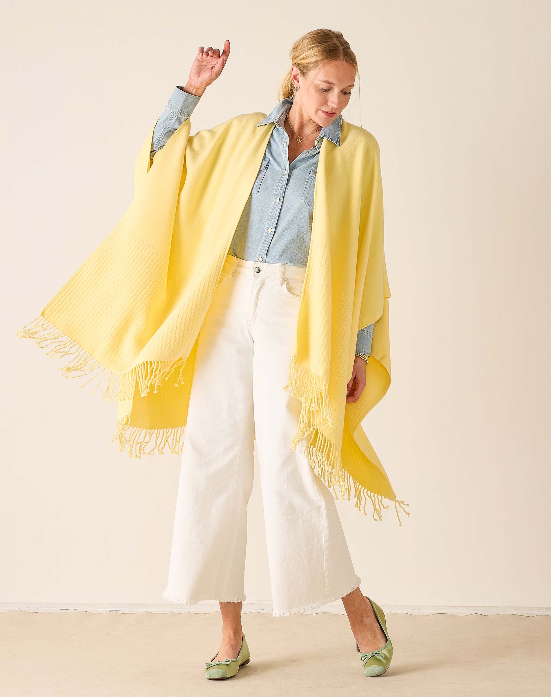 Woman wearing a yellow scarf with white pants and a light blue shirt on a beige background