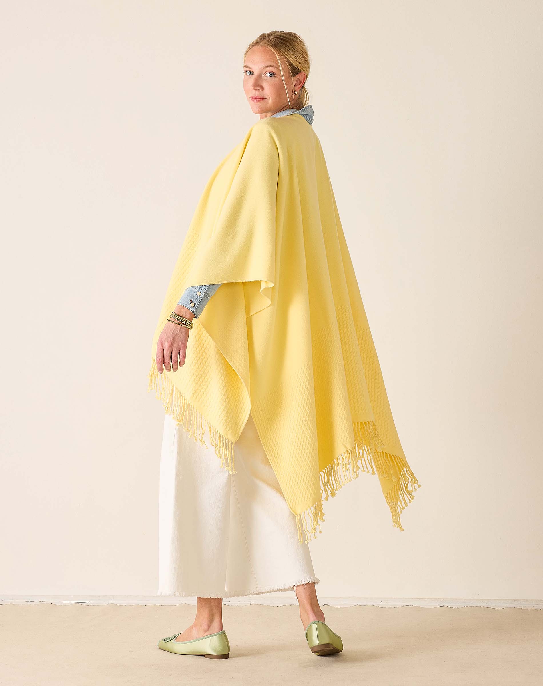 Woman wearing a yellow shawl over a white outfit on a beige background