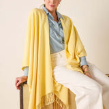 Woman wearing a yellow shawl over a light blue shirt and white pants, sitting on a chair.