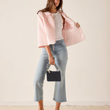 Woman wearing a pink quilted jacket, white shirt, blue jeans, and yellow shoes against a beige background