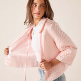 Woman wearing a light pink quilted jacket over a white top and blue jeans on a plain background