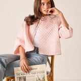 Woman in a pink quilted jacket holding a newspaper on a wooden chair.