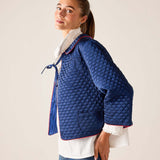 Woman wearing a blue quilted jacket with a white shirt underneath on a plain background
