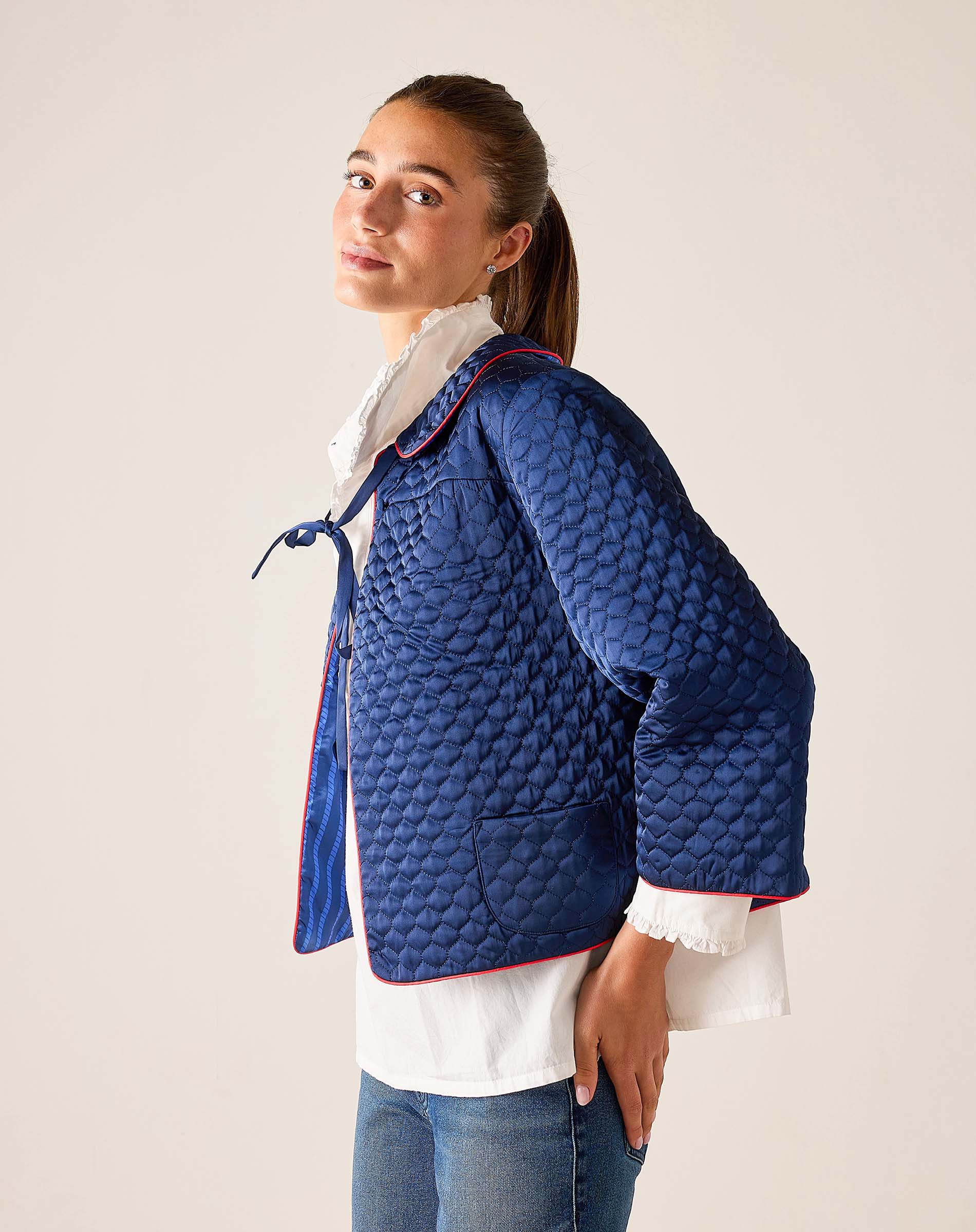 Woman wearing a blue quilted jacket with a white shirt underneath on a plain background