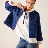 Woman wearing a blue quilted jacket over a white shirt with a neutral background