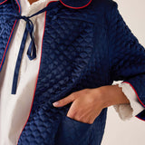 Navy quilted jacket with white and red trim on a neutral background