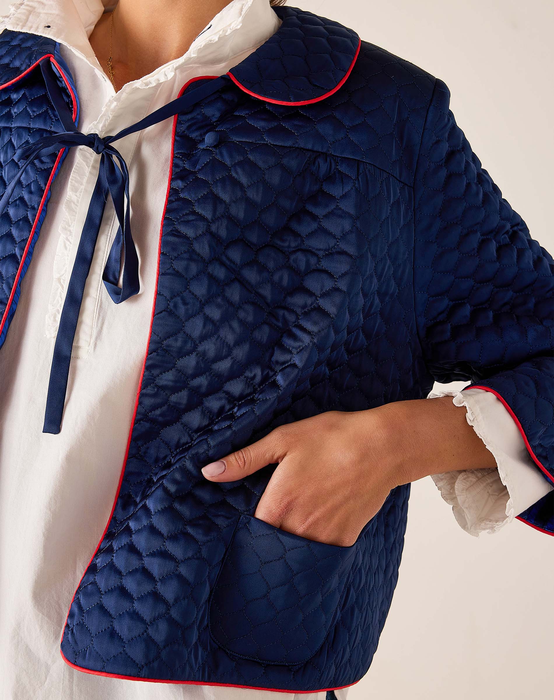 Navy quilted jacket with white and red trim on a neutral background