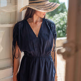 Woman wearing a navy blue dress and straw hat standing outdoors.