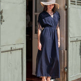 Woman in a navy dress and wide-brimmed hat standing in a doorway.