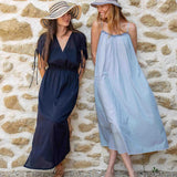 Two women in dresses standing against a stone wall.