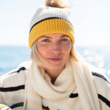 Cream and mustard yellow striped knit beanie with a large yarn pom-pom.