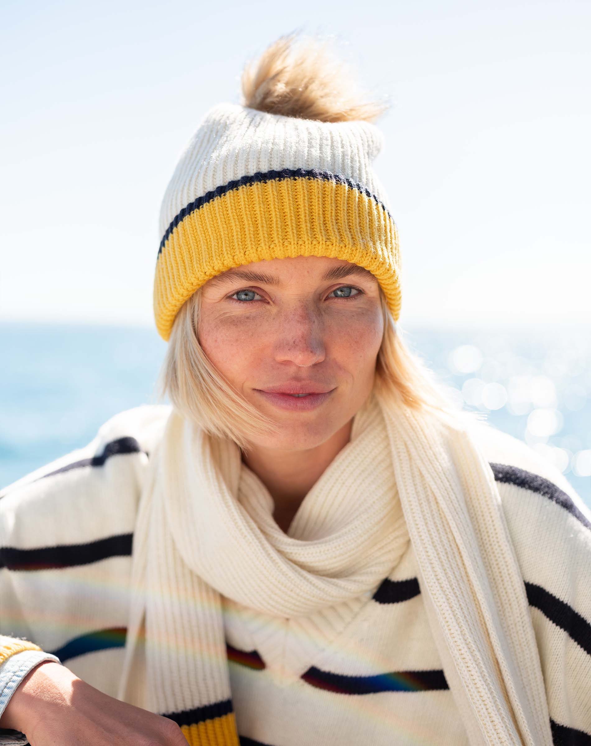Cream and mustard yellow striped knit beanie with a large yarn pom-pom.