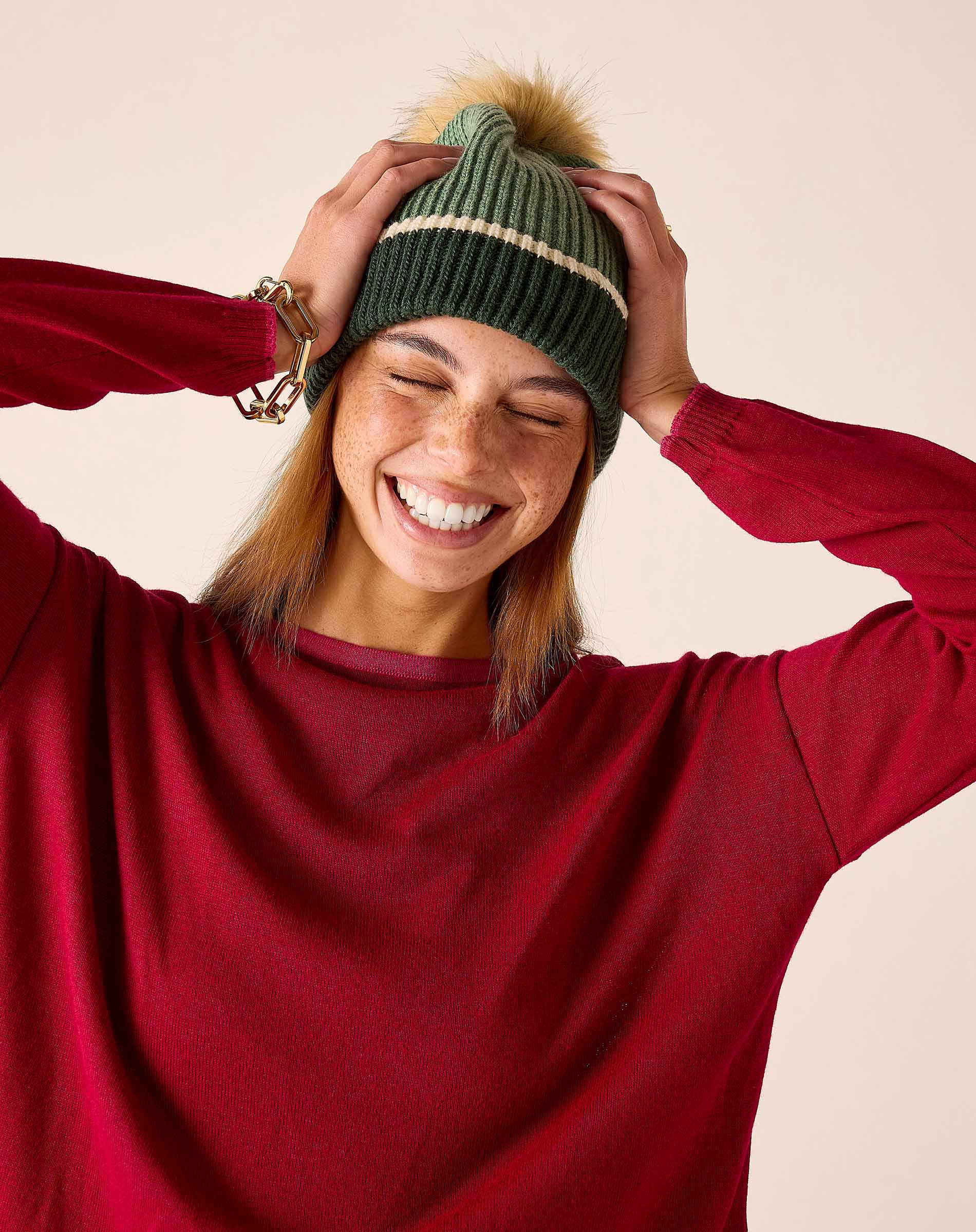 Olive green knit beanie with a decorative stripe and large pom-pom.