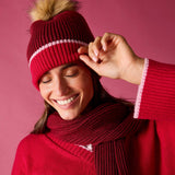 Raspberry pink ribbed knit beanie with a large faux fur pom-pom and white contrast stitching.