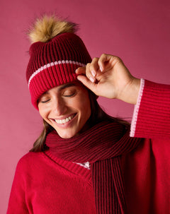 Raspberry pink ribbed knit beanie with a large faux fur pom-pom and white contrast stitching.