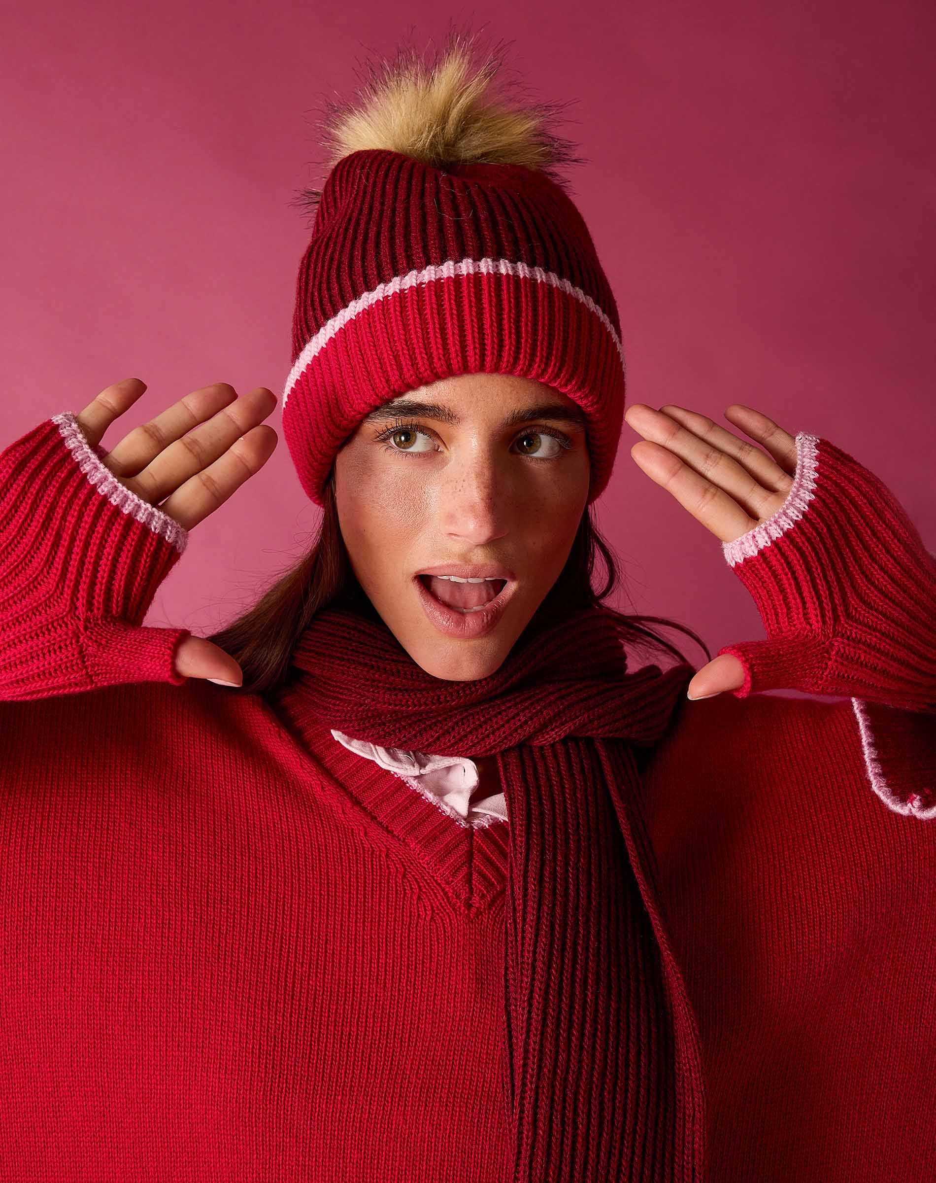 Raspberry pink knit beanie with a large faux fur pom-pom and ribbed texture.
