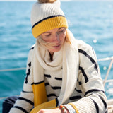 Cream and golden yellow striped knit scarf draped over a chunky knit sweater.