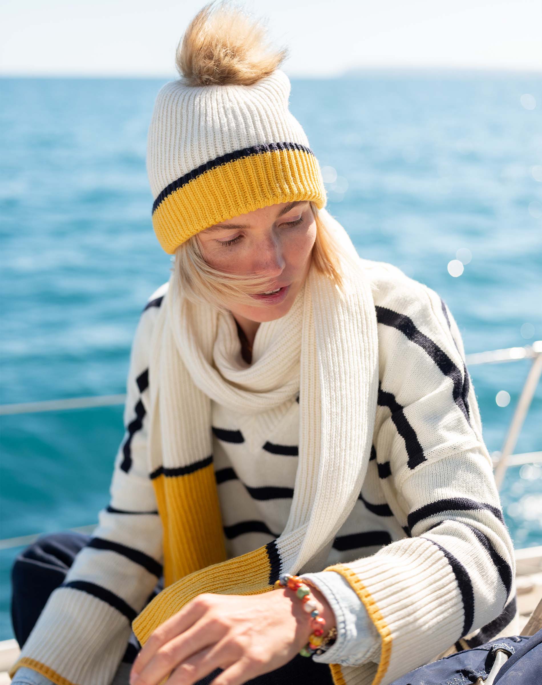 Cream and golden yellow striped knit scarf draped over a chunky knit sweater.
