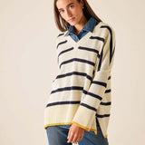 Cream knit v-neck top with navy stripes and a yellow hem over blue jeans.