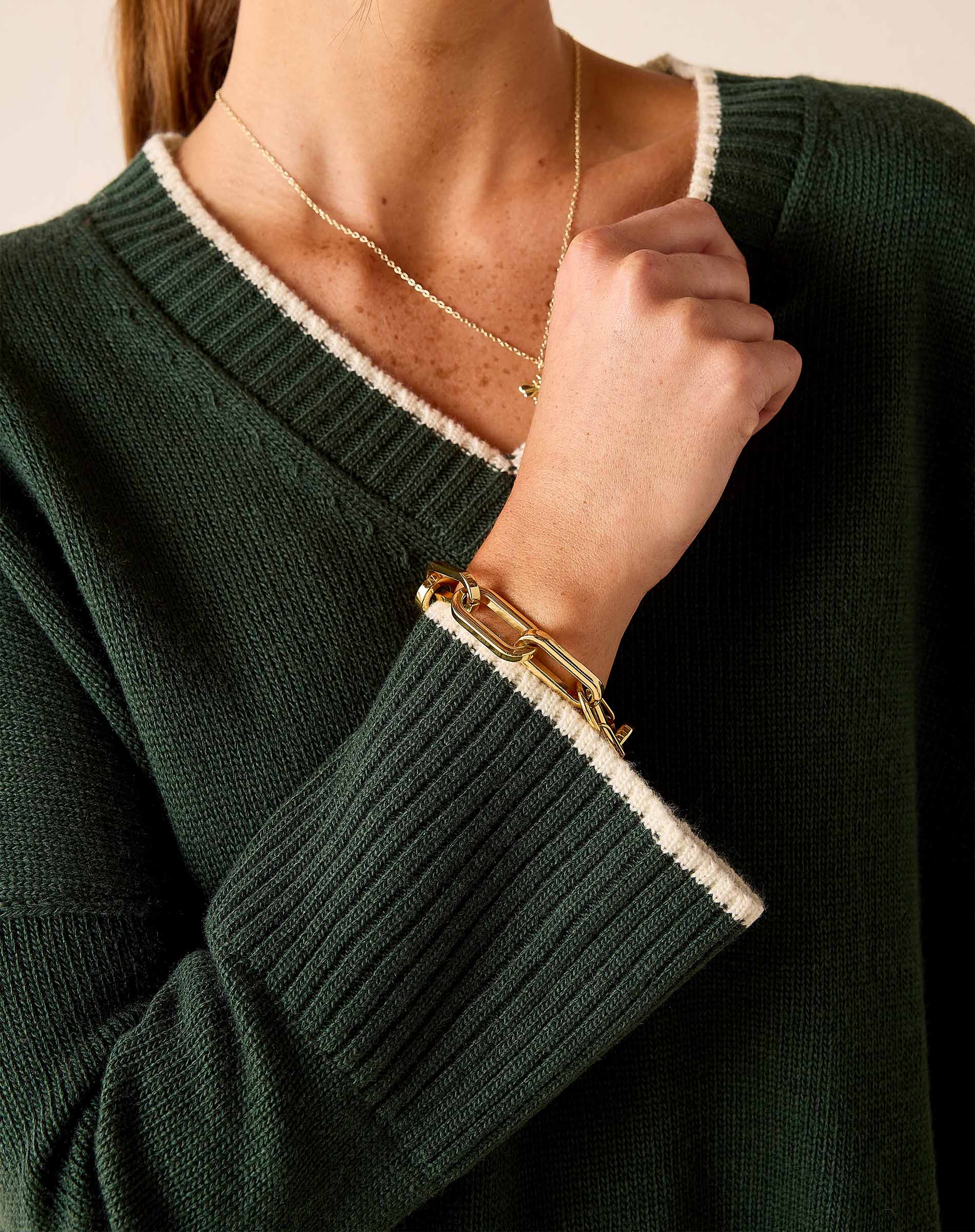 Dark green ribbed knit v-neck sweater with white trim and gold jewelry