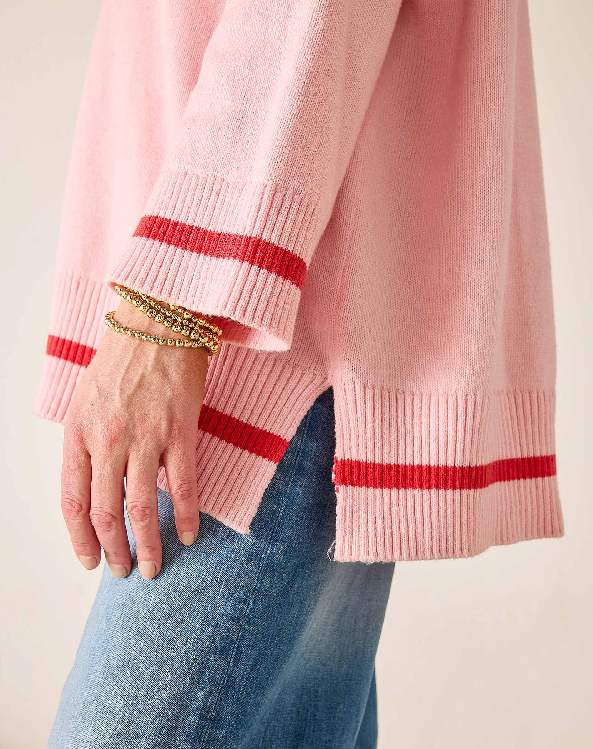 Pink sweater with red stripes worn by a person, with a focus on the sleeve and hand.