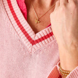 Person wearing a pink sweater with red trim, gold necklace, and bracelet.