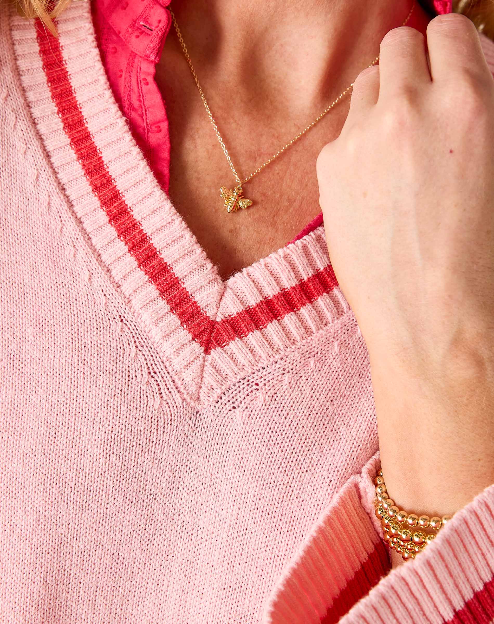 Person wearing a pink sweater with red trim, gold necklace, and bracelet.