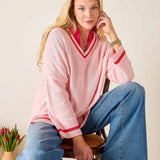 Woman wearing a pink sweater with red trim and blue jeans sitting on a chair.